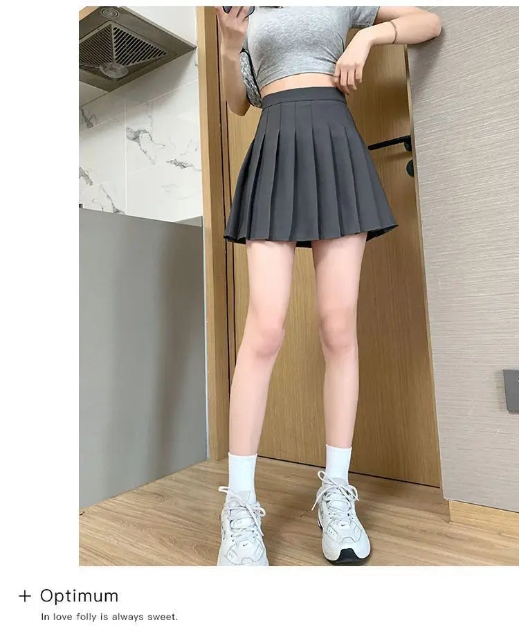 Liveify black pleated tennis skirt with high waist, worn with gray crop top and white sneakers