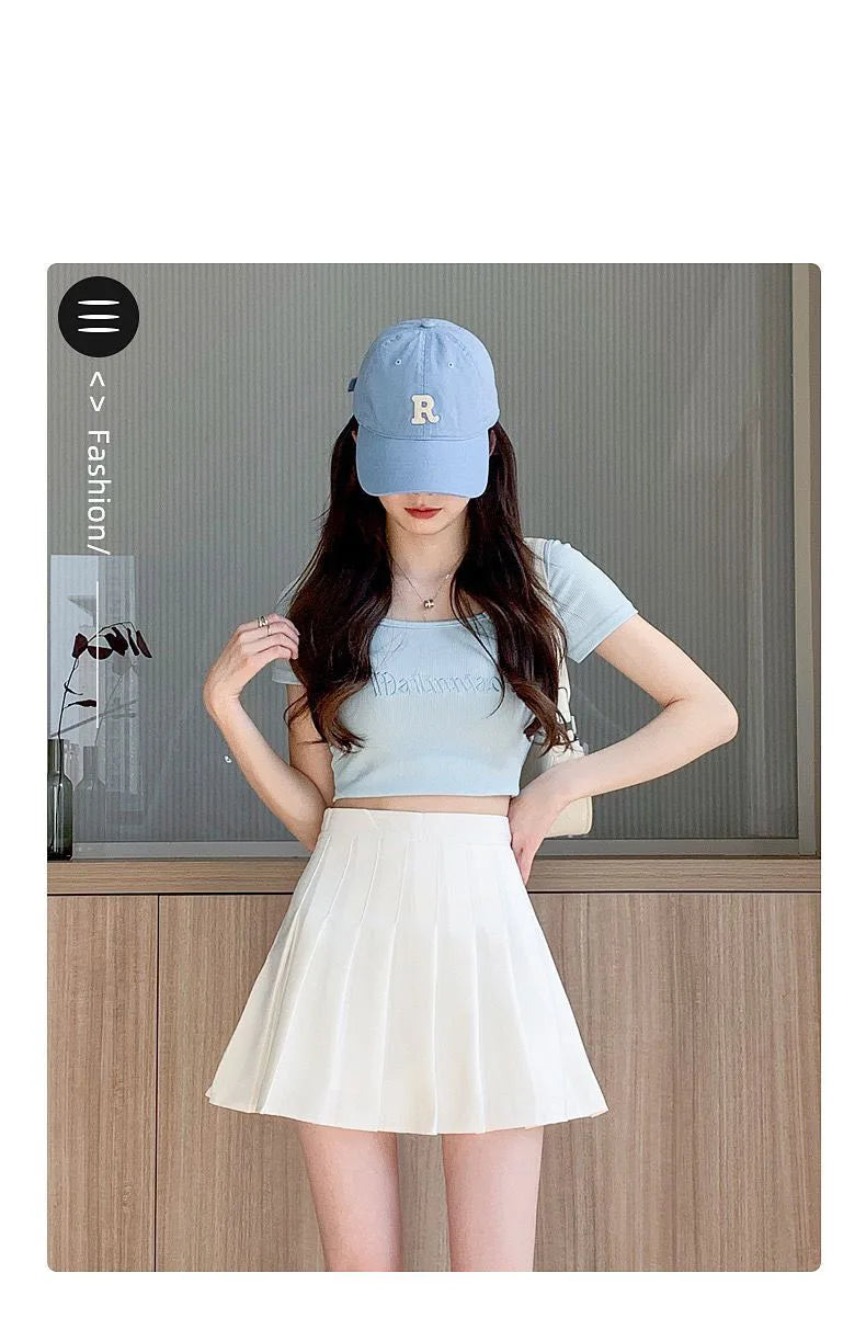 Liveify light blue baseball cap with embroidered R, worn with crop top and white pleated skirt