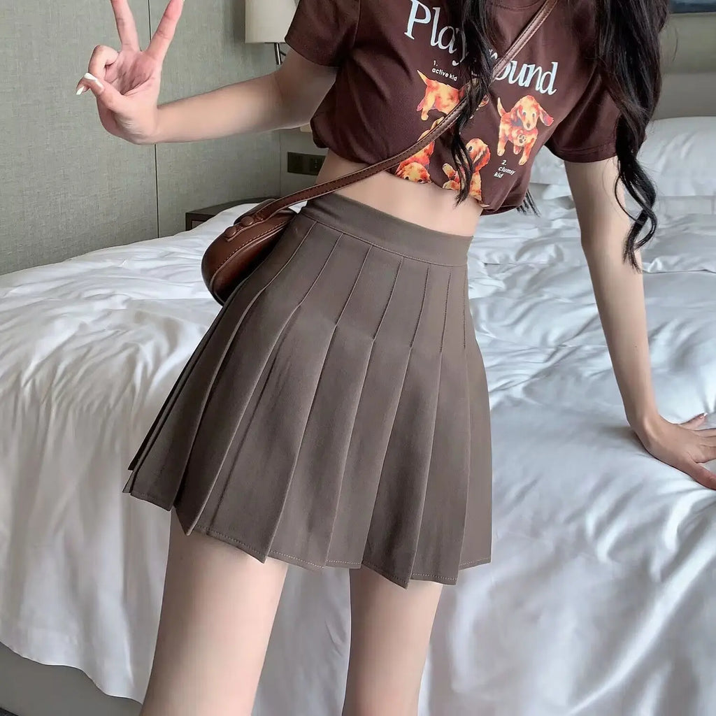 Liveify brown pleated mini skirt with high waist, worn with graphic tee and crossbody bag