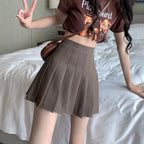 Liveify brown pleated mini skirt with high waist, worn with graphic tee and crossbody bag