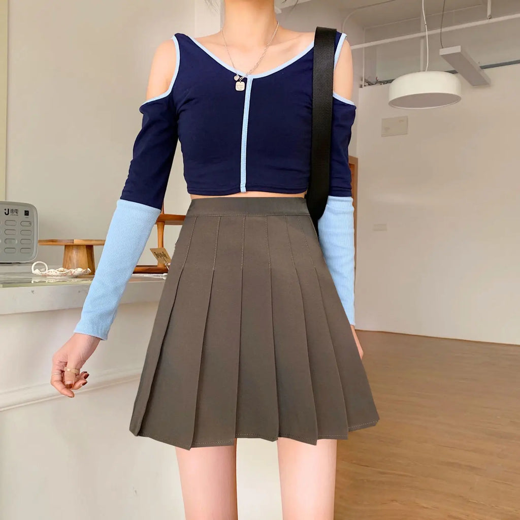 Liveify olive green pleated tennis skirt with navy blue cold-shoulder crop top, light blue ribbed sleeves, casual outfit