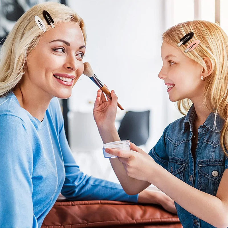 Liveify mother and daughter applying makeup with brushes, wearing hair clips, casual home setting