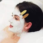 Liveify woman with white face mask in bubble bath, hair held back by gold clips, beauty skincare routine
