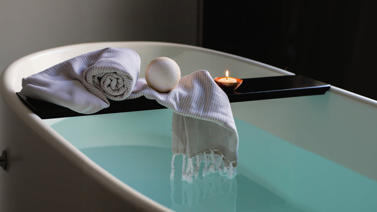 Relaxing bath with towels, soap, and a candle in a dimly lit room.
